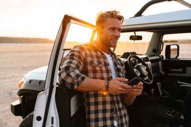 Kumsalın kapısında durup mesajlaşırken cep telefonu kullanan yakışıklı bir genç.