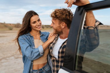 Birbirleriyle kaynaşırken ve arabalarına yaslanırken gülümseyen güzel bir çift.