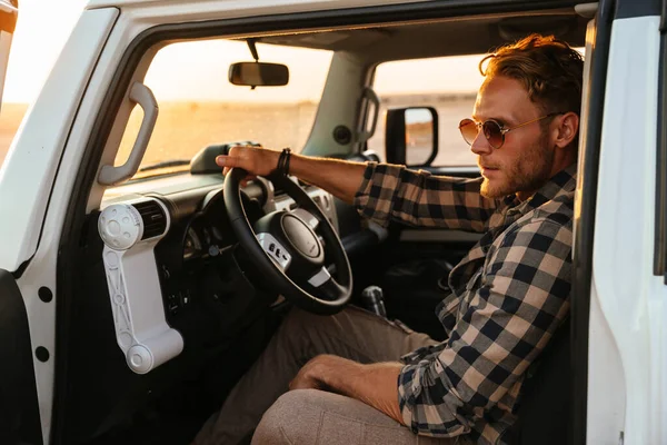 stock image Attractive young man sitting on a front sit in hos car at the beach, open door