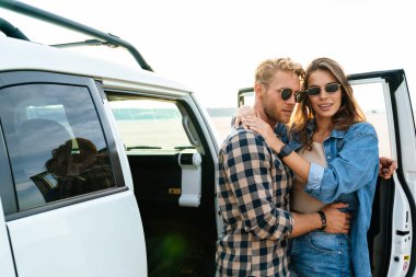 Birbirleriyle kaynaşırken ve arabalarına yaslanırken gülümseyen güzel bir çift.