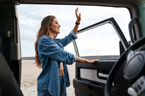 Szczęśliwa Młoda Kobieta Stojąca Przy Drzwiach Samochodu Machająca Ręką Plaży — Zdjęcie stockowe