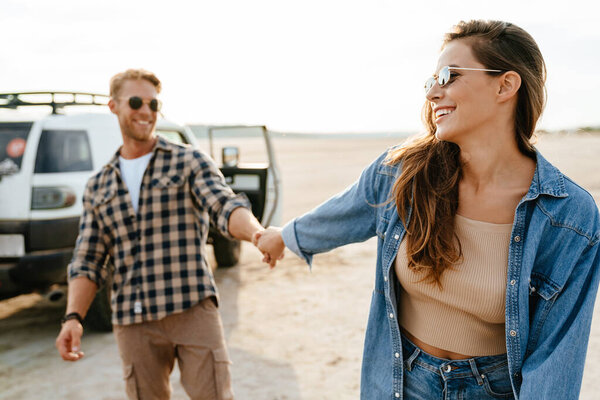 Young happy loving couple outdoors at beach near car walking, embracing, holding hands