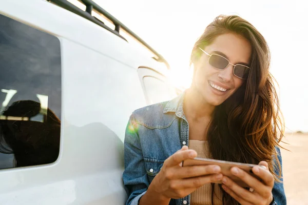 Приваблива Молода Жінка Спираючись Машину Стоїть Пляжі Використовуючи Мобільний Телефон — стокове фото