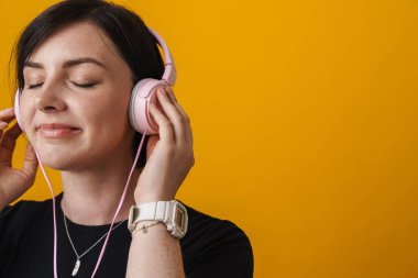 Sarı arka planda izole edilmiş kulaklıkla müzik dinleyen genç bir kadının portresi.