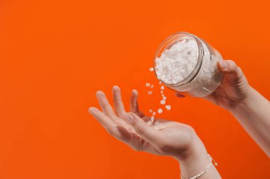 Kadının elleri arka planda deniz tuzu bulunan kavanozu gösteriyor.