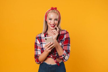 Sarı arka planda izole edilmiş cep telefonu kullanan neşeli sarışın poster kızı