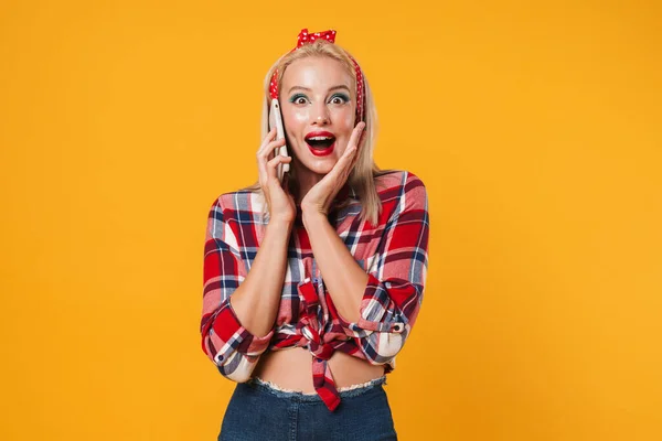 驚きのブロンドPinup女の子話しています上の携帯電話絶縁上の黄色の背景 — ストック写真