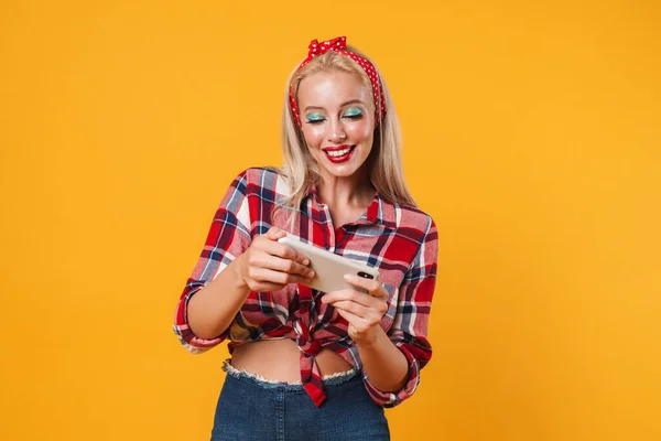 興奮したブロンドのピンアップ女の子のイメージは黄色の背景上に隔離された携帯電話でオンラインゲームをプレイ — ストック写真
