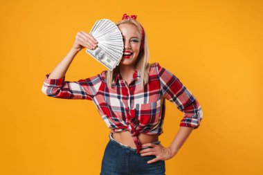 Sarı arka planda izole edilmiş dolarlarla poz veren neşeli sarışın kız resmi