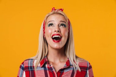 Heyecanlı sarışın poster kızı görüntüsü. Sarı arka planda yalnız poz veriyor ve yukarı bakıyor.