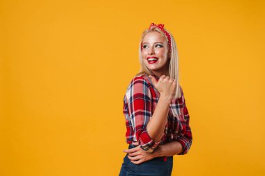 Sarı arka planda izole edilmiş, gülümseyen ve işaret eden neşeli sarışın kız resmi