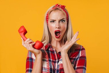 Sarı arka planda izole edilmiş cep telefonuyla poz veren şok olmuş güzel bir kız resmi