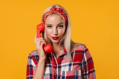 Sarı arka planda izole edilmiş, cep telefonuyla poz veren güzel bir kız resmi