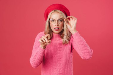 Şok olmuş güzel kız öğrencinin pembe arka planda izole edilmiş kamerayı işaret etmesi.