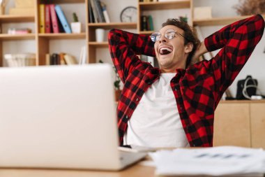 Ofiste dizüstü bilgisayarla çalışırken gözlüklü yakışıklı adam esniyor.