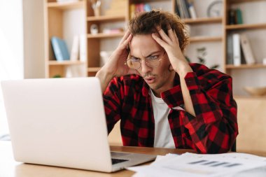 Gözlüklü yakışıklı adam ofiste otururken dizüstü bilgisayarla çalışıyor.