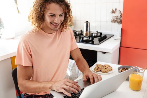 Caucasiano Bonito Sorrindo Cara Usando Laptop Enquanto Toma Café Manhã — Fotografia de Stock