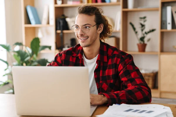 Bonito Sorrindo Cara Óculos Trabalhando Com Laptop Enquanto Sentado Escritório — Fotografia de Stock