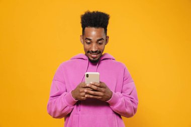 Gülümseyen ve sarı arka planda cep telefonu kullanan neşeli Afrikalı Amerikalı adam.