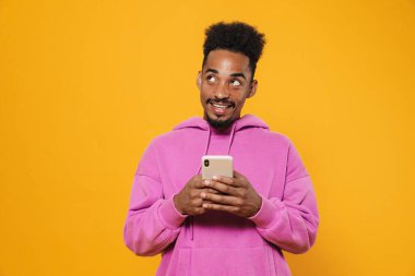 Gülümseyen ve sarı arka planda cep telefonu kullanan neşeli Afrikalı Amerikalı adam.