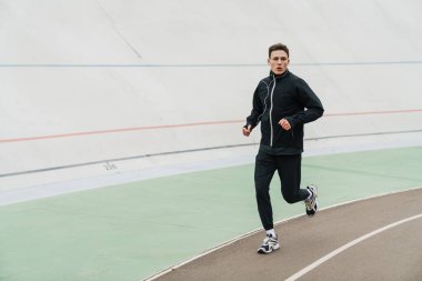 Stadyumda koşup kulaklıkla müzik dinleyen kendine güvenen genç bir adam.