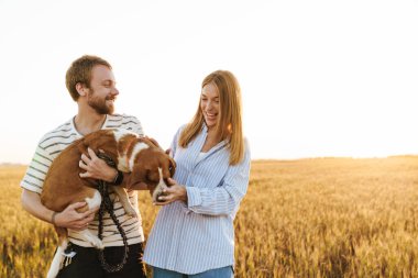 İyimser, genç ve sevgi dolu bir çiftin dışarıda köpekle yürüdüğü bir fotoğraf.
