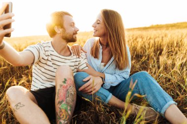 Sahada cep telefonuyla selfie çeken neşeli, pozitif bir çiftin görüntüsü.