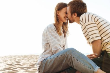 Sahilde oturmuş öpüşen genç bir çiftin görüntüsü.