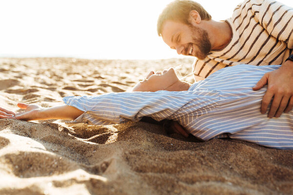 Изображение молодой позитивной любящей пары, лежащей на пляже обнимающей