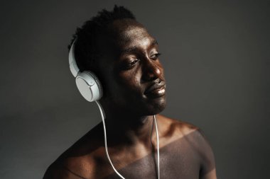 Gri arka planda tek başına çalışırken kulaklık kullanan Afro-Amerikan sporcusu.