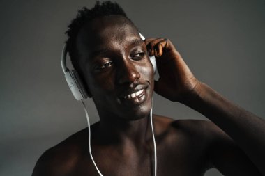 Gülümseyen Afro-Amerikan sporcusu gri arka planda tek başına çalışırken kulaklık kullanıyor.