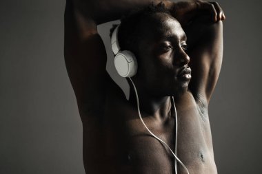 Gömleksiz Afro-Amerikan sporcusu, kulaklık takıp kollarını geriyor. Gri arka planda izole bir şekilde.