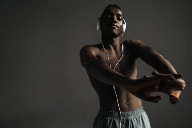 Tişörtsüz Afro-Amerikan sporcusu kulaklık takıyor ve ellerini arka planda kapalı tutuyor.