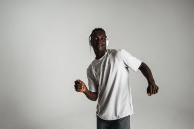 Gülümseyen Afrikalı Amerikalı adam kulaklıkla müzik dinliyor ve beyaz arka planda yalnız dans ediyor.