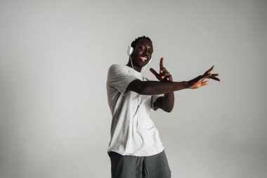 Gülümseyen Afrikalı Amerikalı adam kulaklıkla müzik dinliyor ve beyaz arka planda yalnız dans ediyor.