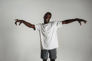 Gülümseyen Afrikalı Amerikalı adam kulaklıkla müzik dinliyor ve beyaz arka planda yalnız dans ediyor.