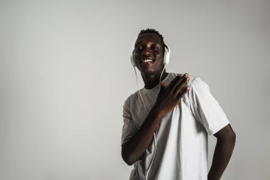 Gülümseyen Afrikalı Amerikalı adam kulaklıkla müzik dinliyor ve beyaz arka planda yalnız dans ediyor.
