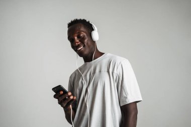 Beyaz arka planda izole edilmiş kulaklık ve cep telefonuyla müzik dinleyen mutlu Afrikalı Amerikalı adam.