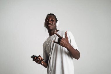 Beyaz arka planda izole edilmiş kulaklık ve cep telefonuyla müzik dinleyen mutlu Afrikalı Amerikalı adam.