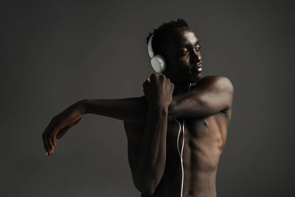 Shirtless african american sportsman using headphones while stretching his arm isolated over grey background