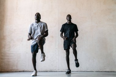 İki genç atletik Afrikalı Amerikalı erkek içeride spor yaparken atlıyorlar.