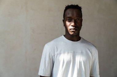 Genç, yakışıklı, ciddi, Afro-Amerikan bir adam duvarın arkasında dikilirken kameraya bakıyor.