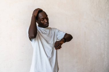 Genç, ciddi, Afro-Amerikan bir adam duvarın içinde dururken kol saatine bakıyor.