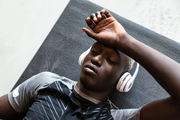 Молодой Атлетичный Афроамериканец Наушниках Лежит Коврике После Тренировки Помещении — стоковое фото