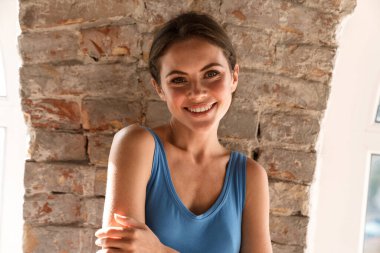 Genç mutlu esmer kadın gülümsüyor ve kapalı alanda kameraya bakıyor.