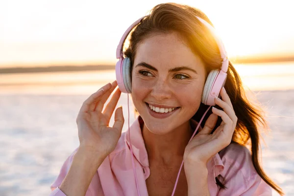 日落时分 一名头戴耳机在海滩上听音乐的松懈女子 正在关门 — 图库照片