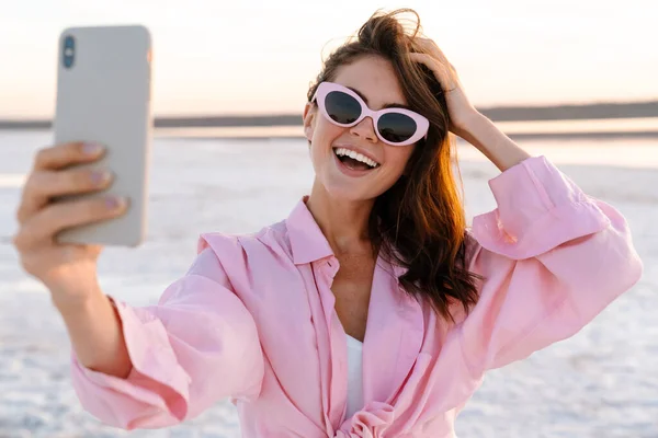 Wesoła Młoda Kobieta Robi Sobie Selfie Stojąc Plaży Podczas Zachodu — Zdjęcie stockowe