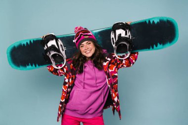 Mavi duvarda izole edilmiş kayakla poz veren mutlu sporcu kadın.