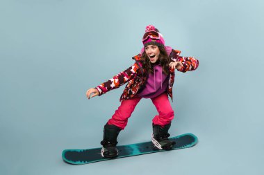 Snowboard 'da poz veren mutlu sporcu kadın mavi duvarın üstünde, ata biniyor.