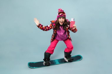 Heyecanlı sporcu kadın, mavi duvarda izole edilmiş bir şekilde pasaportuyla poz veriyor.